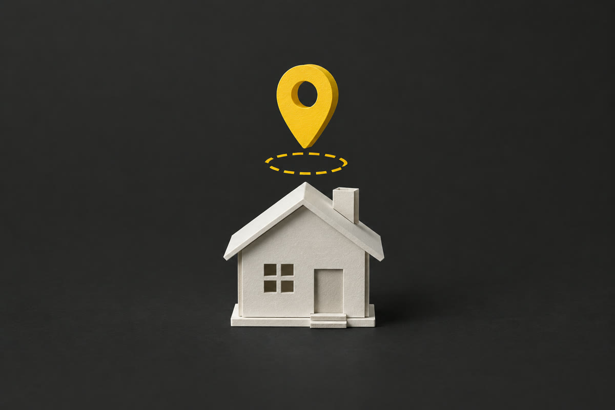 Illustration of a paper house on charcoal with a yellow map pin lifted away above a dashed outline.