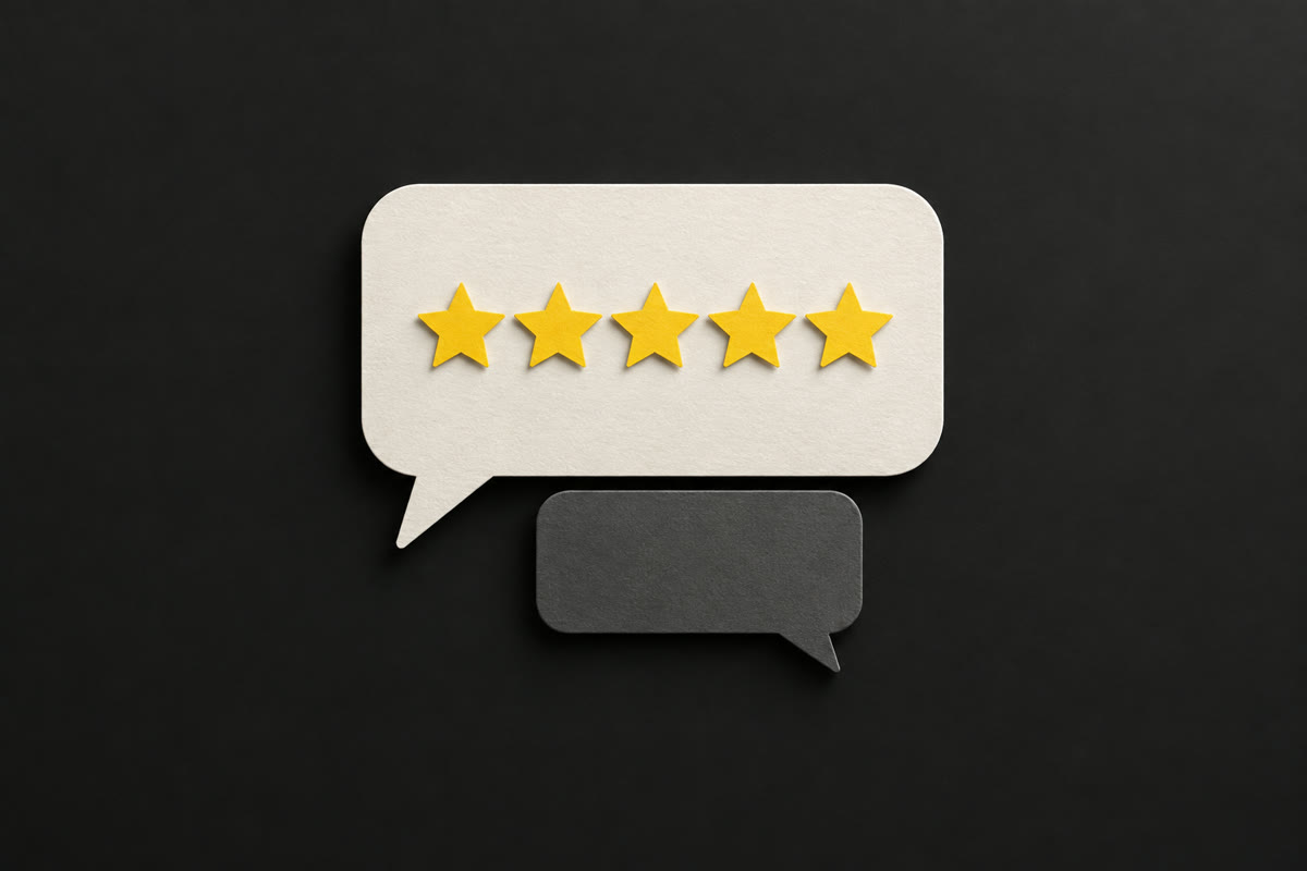 Illustration of an off-white paper speech bubble with five yellow paper stars and a smaller grey reply bubble beneath it, on charcoal.